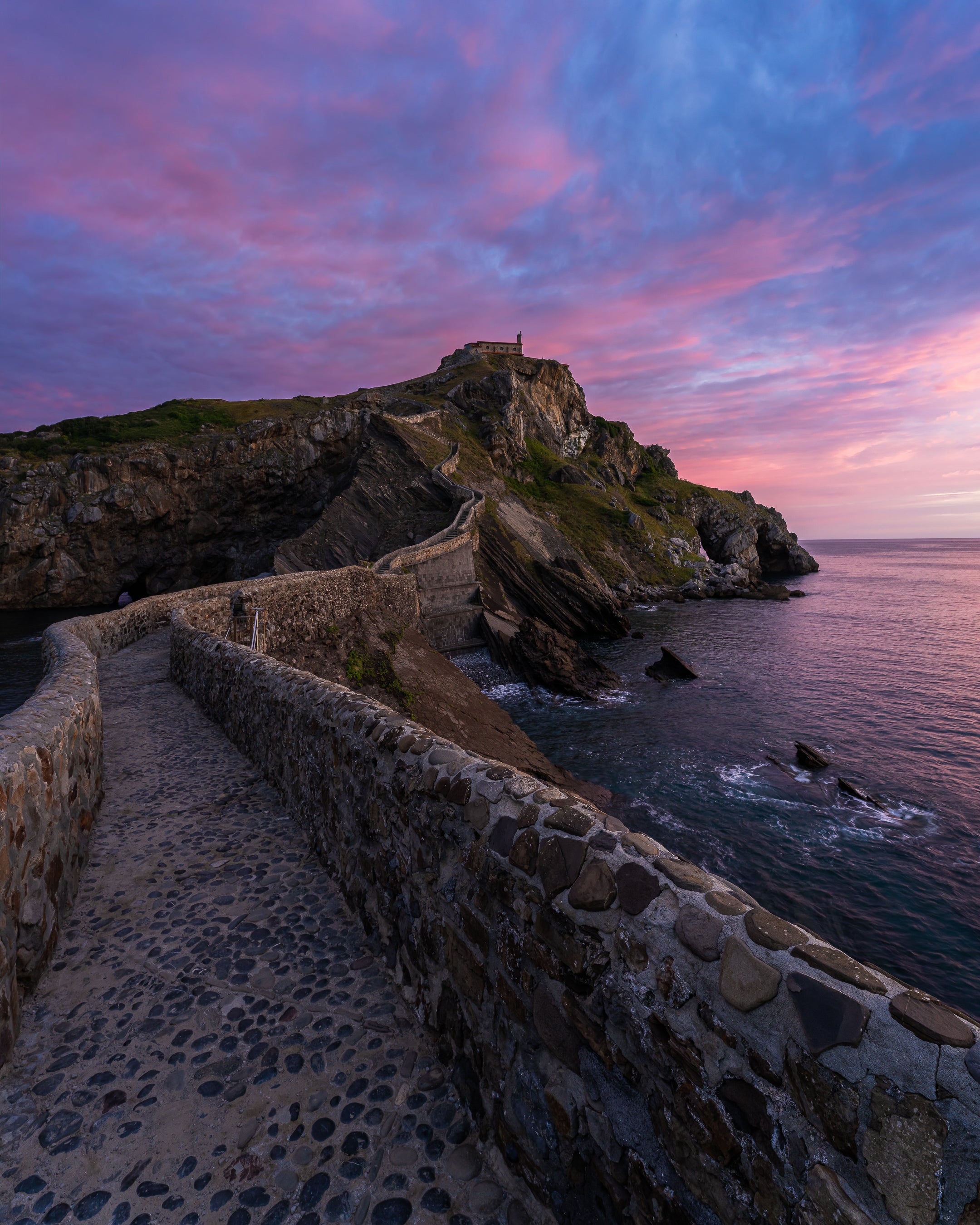 The fortress of Gatzelugatexe appears under a pink sky at sunrise, with the staircase made famous by the Game of Thrones franchise